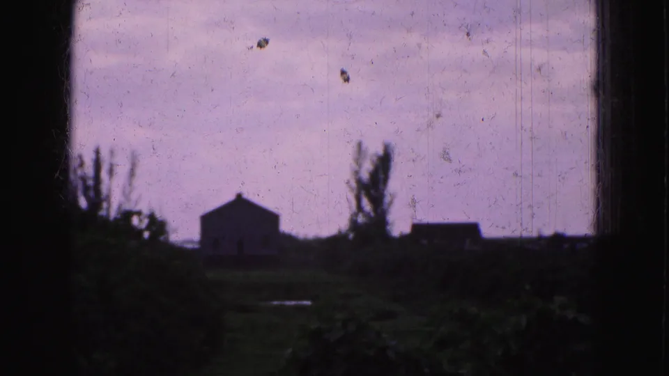 1975 Florida Everglades home-movie frame showing a lone distant house silhouette, trees, grass, and dusky purple sky.