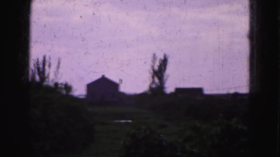 1975 Florida Everglades home-movie view of a distant house-like building, trees, and low vegetation seen through dark frame edges.