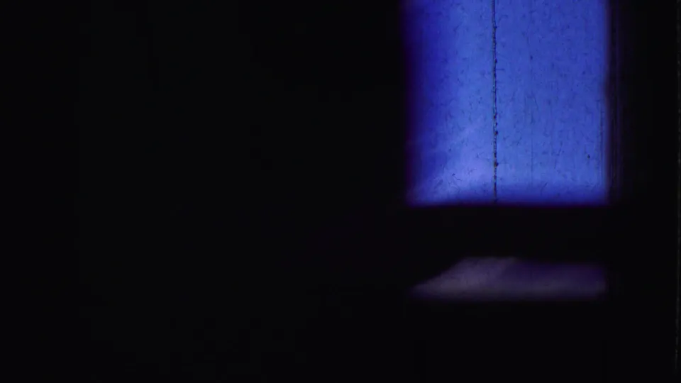 Underexposed 8mm frame from the clip, showing a blue rectangular light patch against mostly black surroundings.