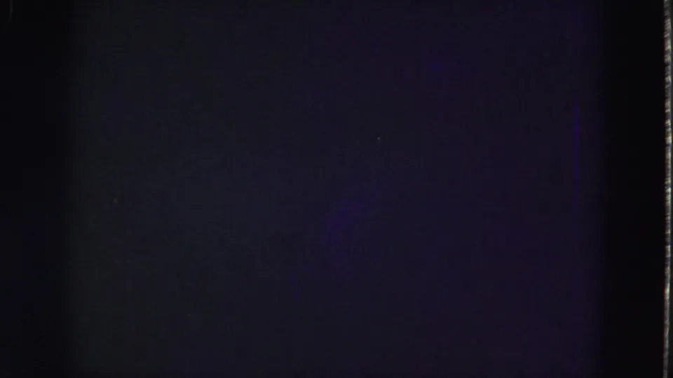 End-of-clip 8mm frame showing mostly darkness with purple-blue fading, grain, and vertical film-edge marks.