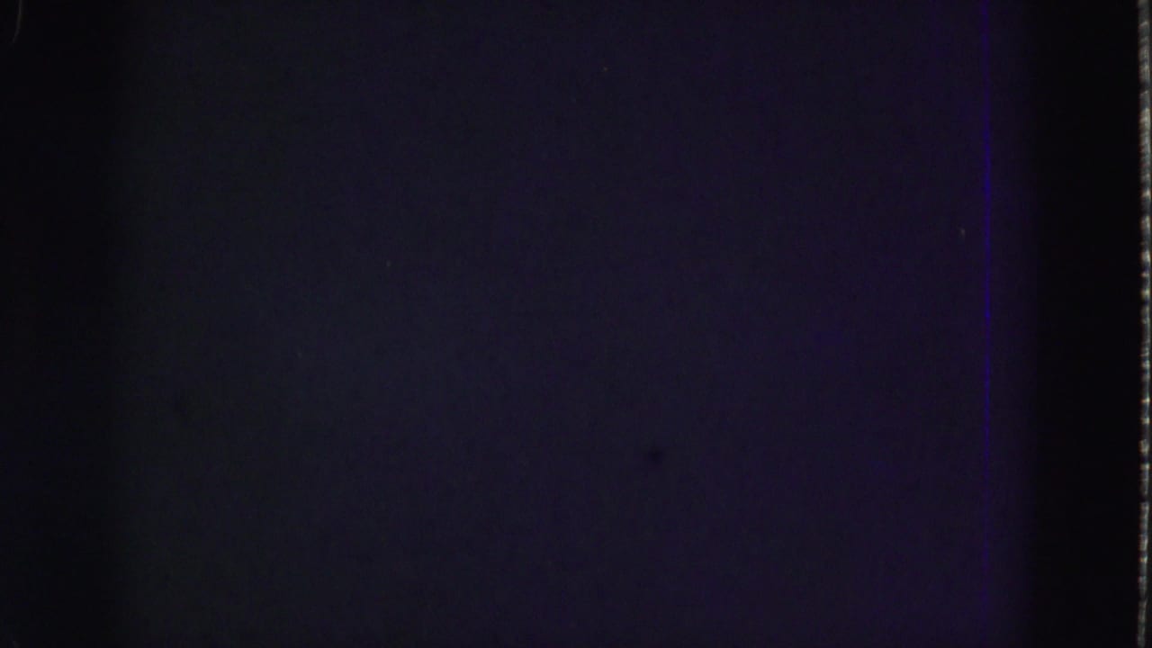 Mostly dark film frame with faint purple cast and visible film edge.