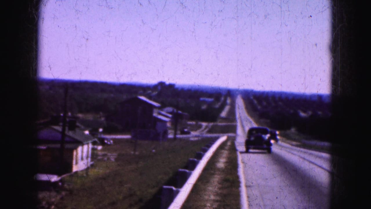 1975 8mm home-movie view of a Florida Everglades road trip, showing cars ahead on a two-lane highway and rural roadside structures.