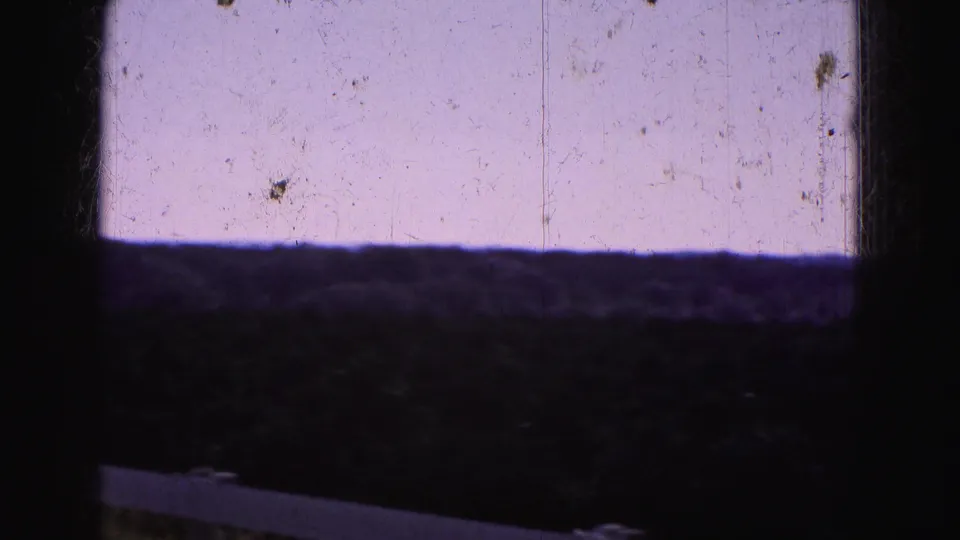 1975 8mm view of a dark agricultural field in the Florida Everglades with a pale sky and partial white fence rail.