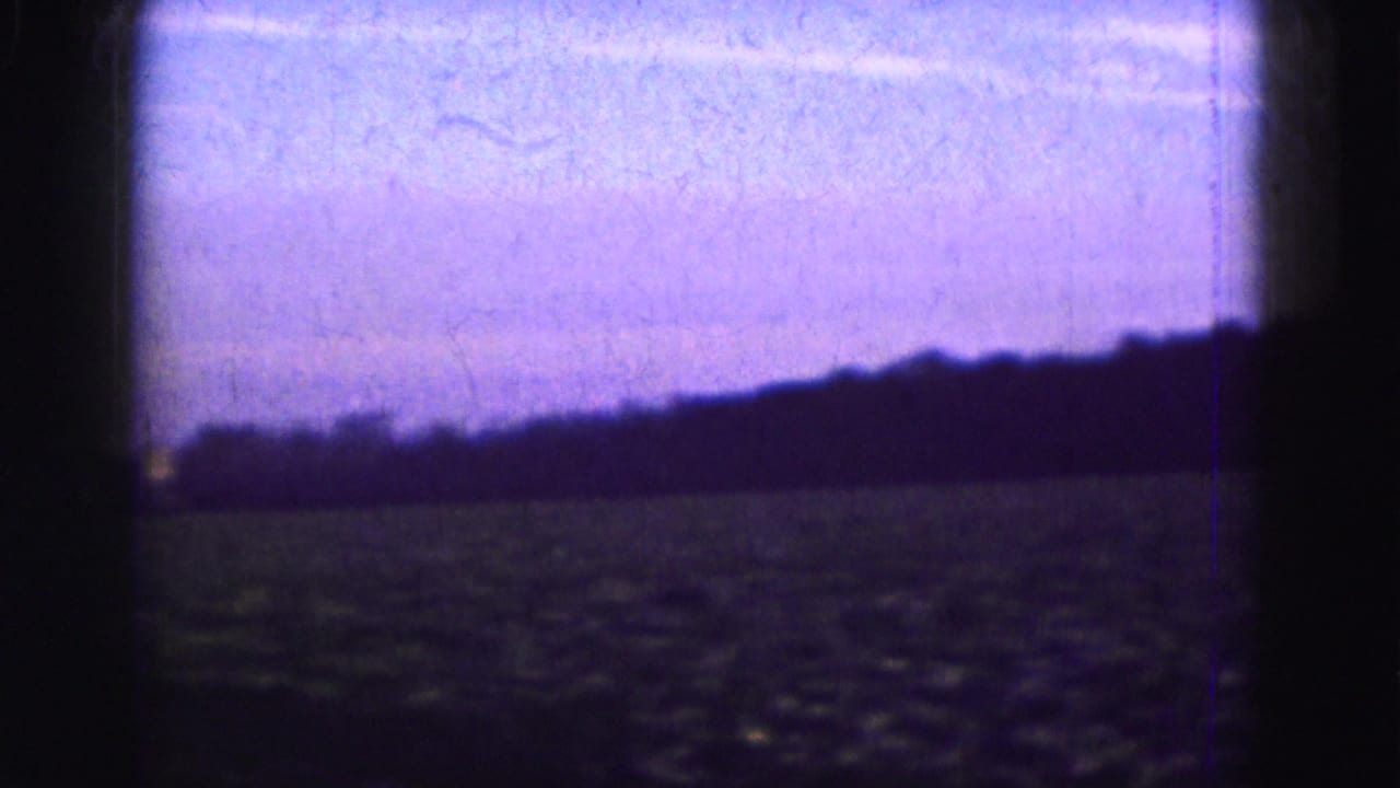 1975 Florida Everglades home-movie frame showing a dark open field, low horizon, and blue-purple sky.