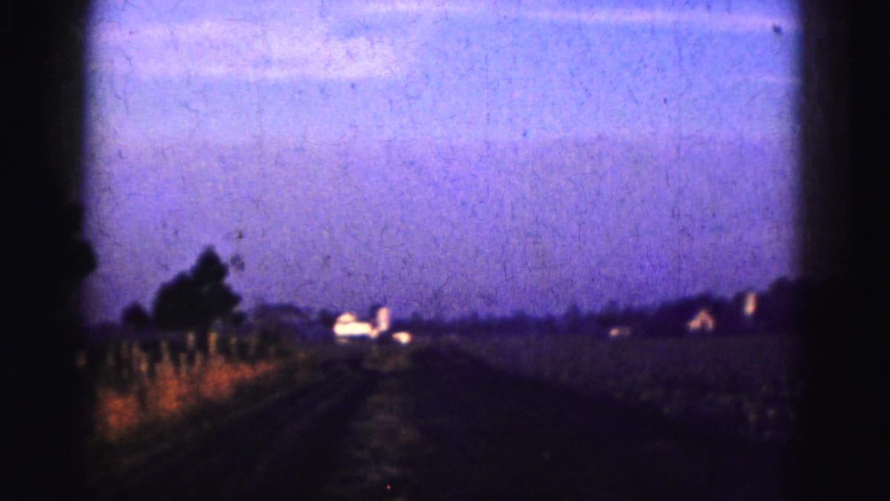 Rural road or track leading toward small distant buildings.