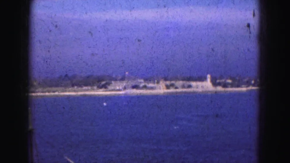 Distant Florida Everglades shoreline across open blue water, with small waterfront structures and a pale tower-like form visible.