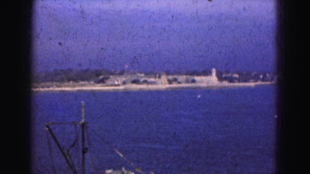 1975 Florida water view with a small fishing or work boat entering below a distant shoreline and hazy sky.