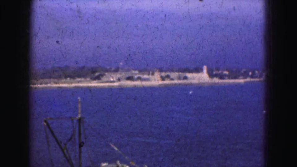 1975 Florida water view with a small fishing or work boat entering below a distant shoreline and hazy sky.