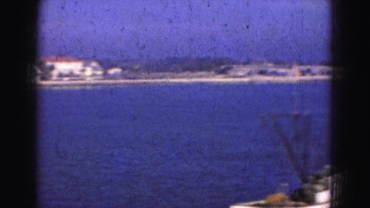 1975 8mm Florida trip view across calm water toward a distant low shoreline with pale waterfront buildings.