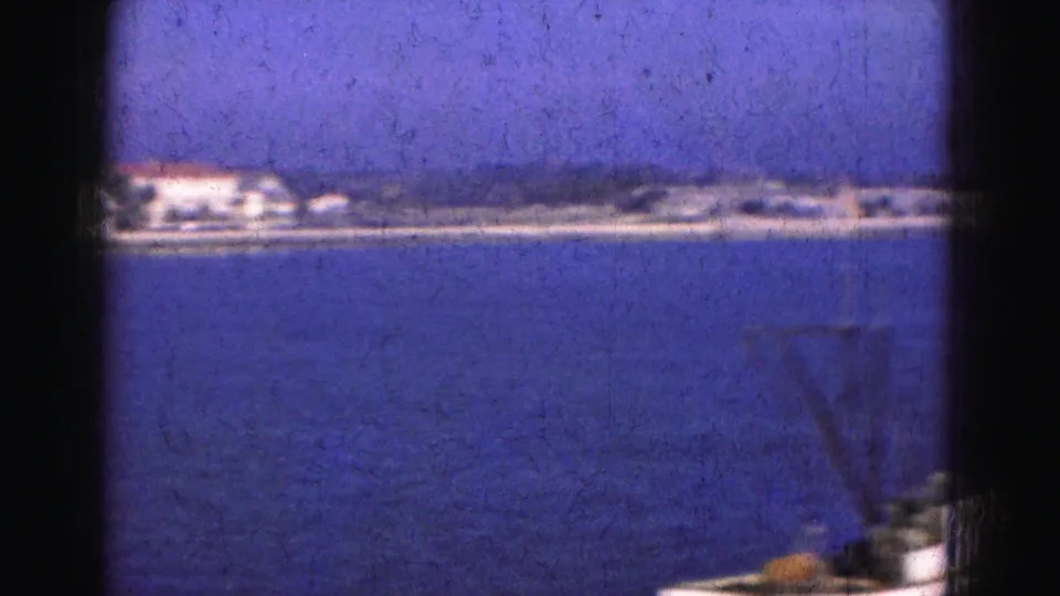 1975 8mm Florida trip view across calm water toward a distant low shoreline with pale waterfront buildings.