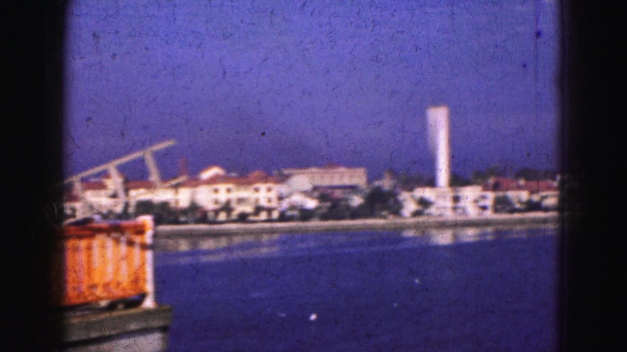 1975 8mm Florida shoreline view with white buildings, a tall tower, and a red-orange dockside object in the foreground.
