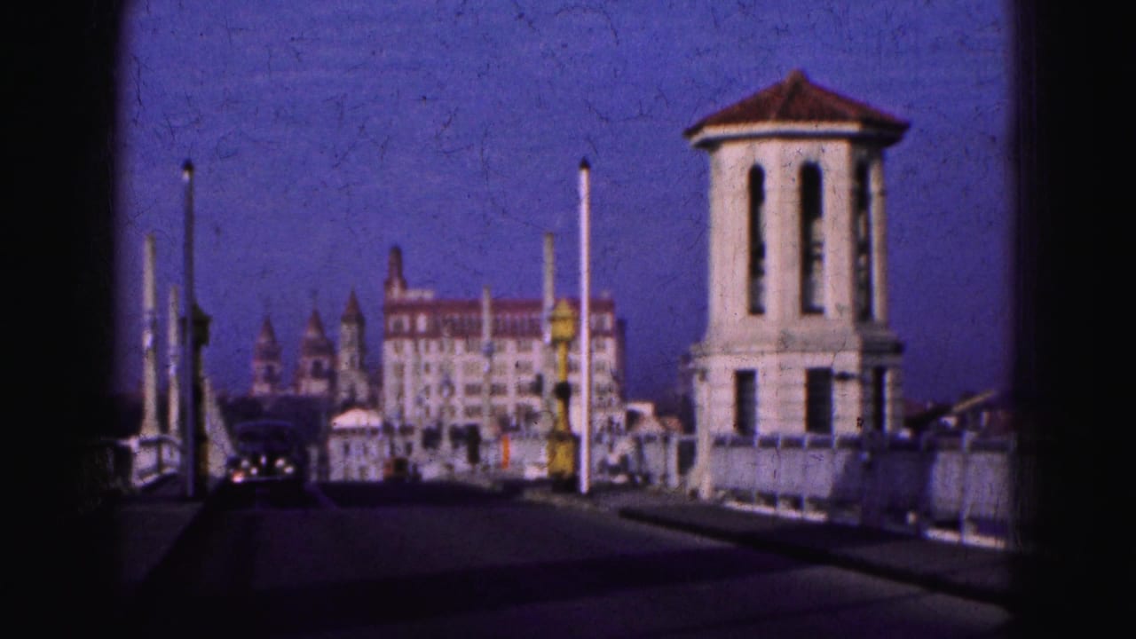 Roadway between pale towers with a distant building, poles, cars, and a yellow signal light.