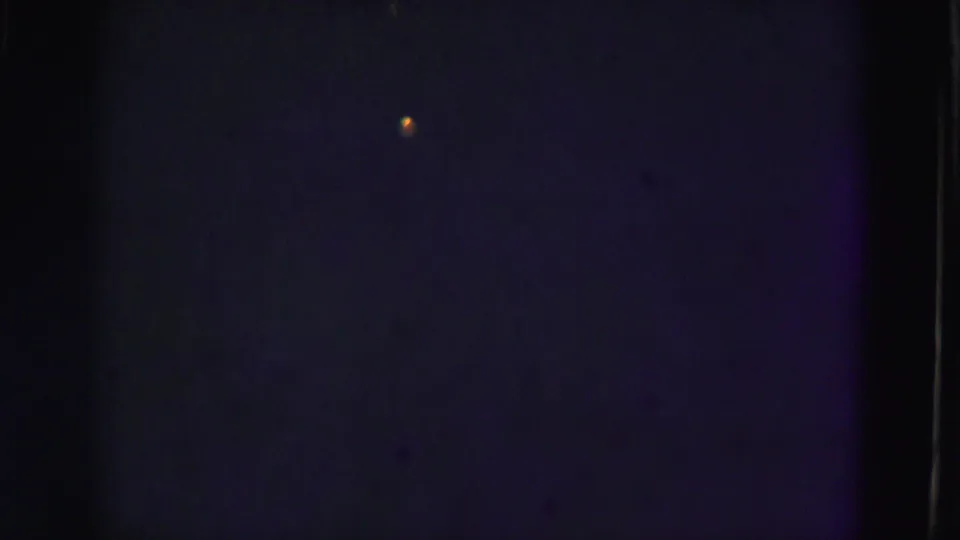 1975 Florida Everglades 8mm frame showing mostly dark blue underwater texture, a small orange speck, and vertical film-edge shadow.