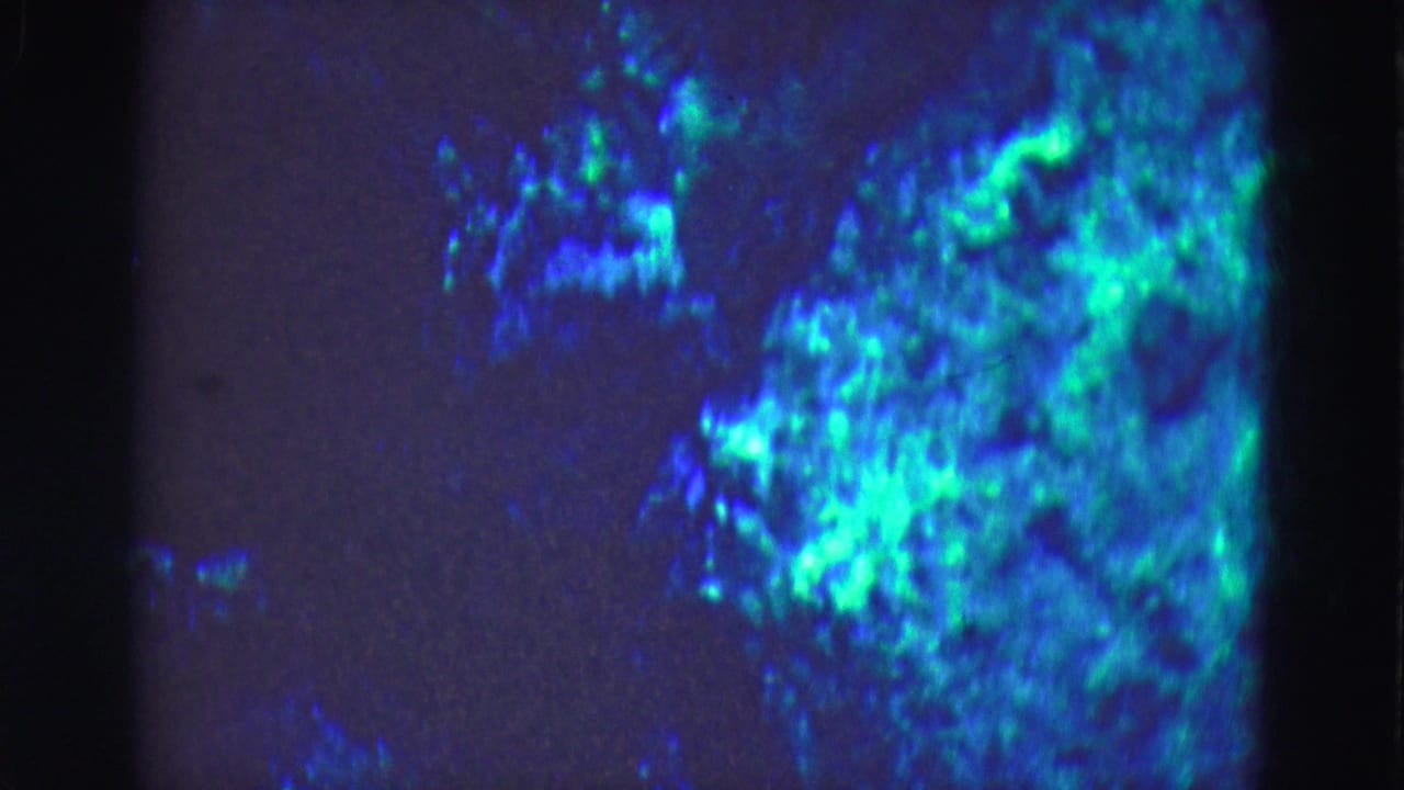 1975 Florida Everglades 8mm underwater frame showing bright turquoise light blooms across blue water, with grain and dark gate edges.