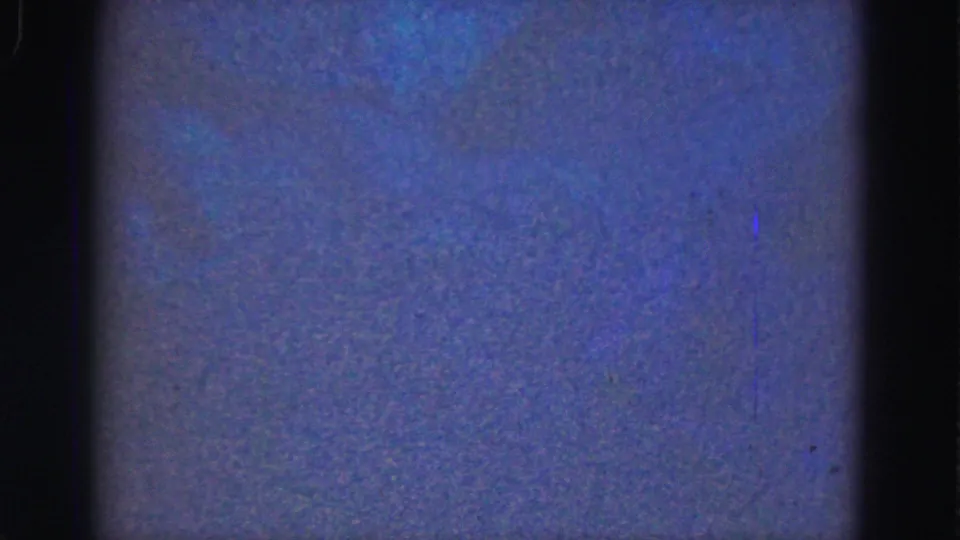 1975 Florida Everglades home-movie frame showing a soft blue aquarium or tank view with faint turquoise patches and dark framing.