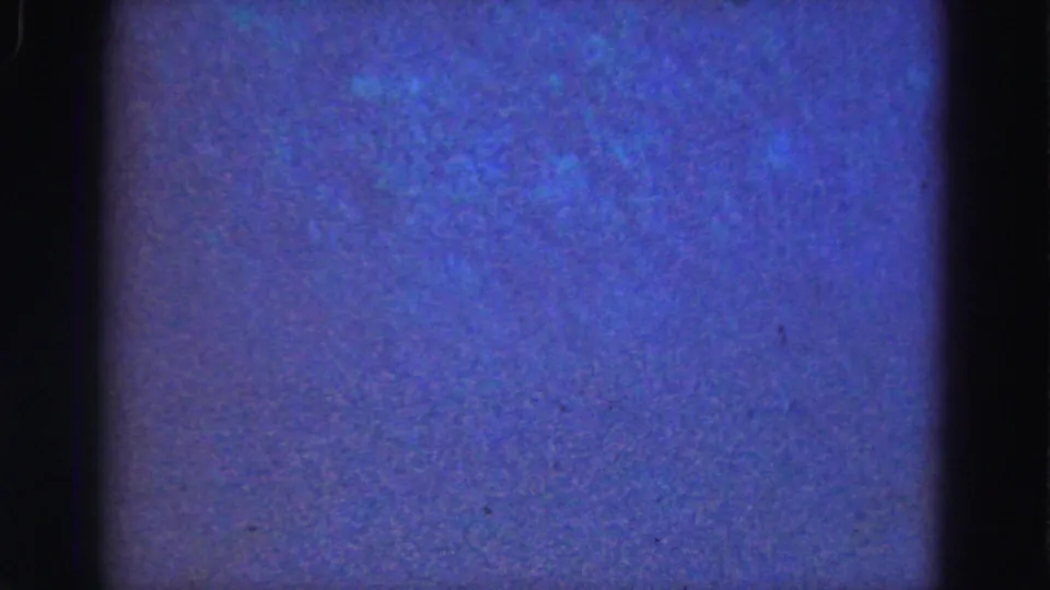 Soft 1975 8mm aquarium view with blue water, faint fish silhouettes, and a bright turquoise patch near the edge.