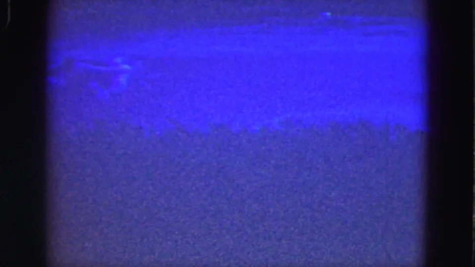 1975 Florida Everglades 8mm frame showing abstract blue light, purple grain, dark gate borders, and faint surface marks without people or landmarks.