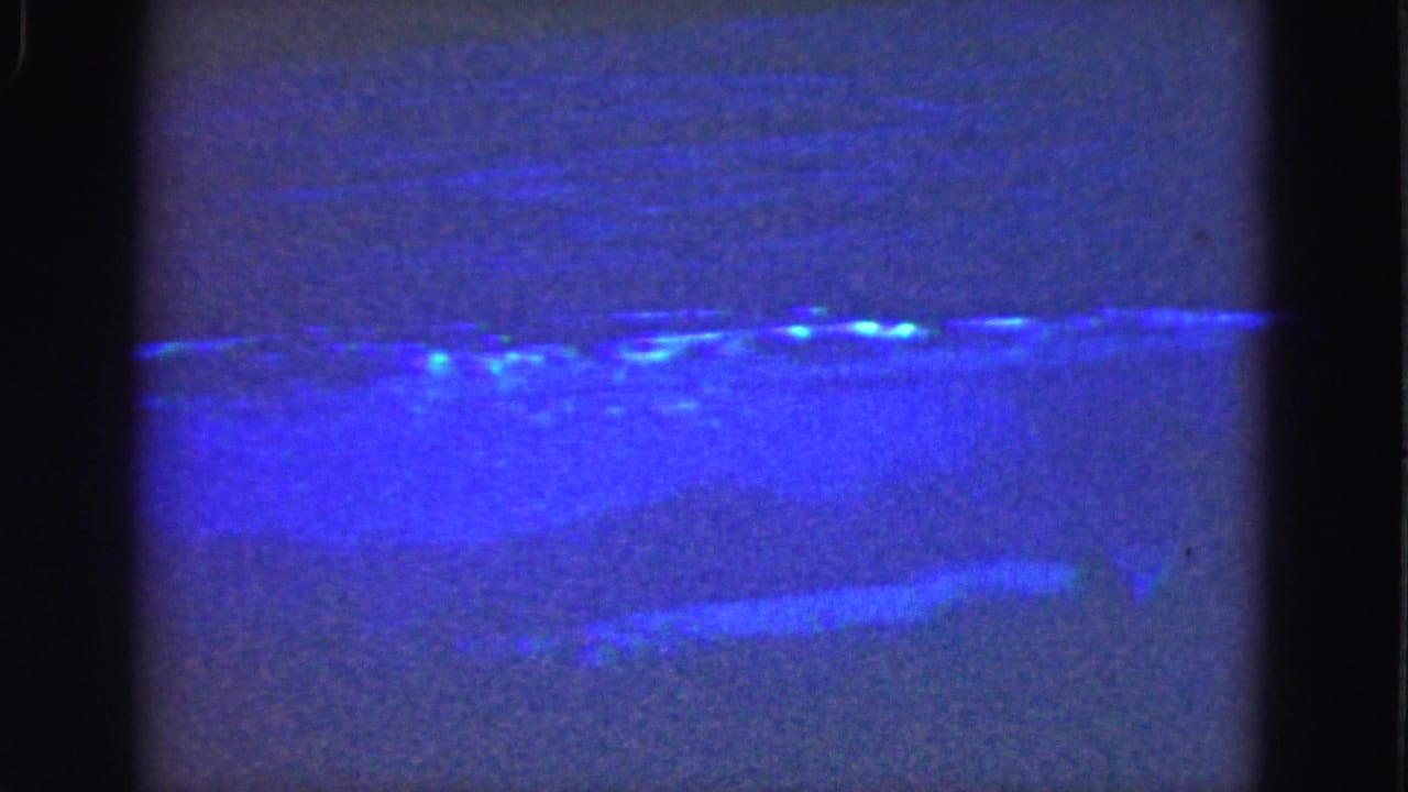 Dim blue shoreline with bright specks near the upper water edge.