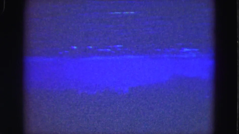 Closing 8mm frame from the Florida Everglades showing a pale blue horizontal band over dark, grainy nighttime water.