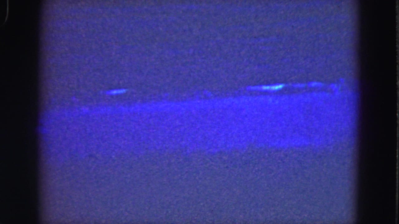 1975 Florida Everglades frame with a hazy blue water surface, faint shoreline, and visible 8mm gate edges.