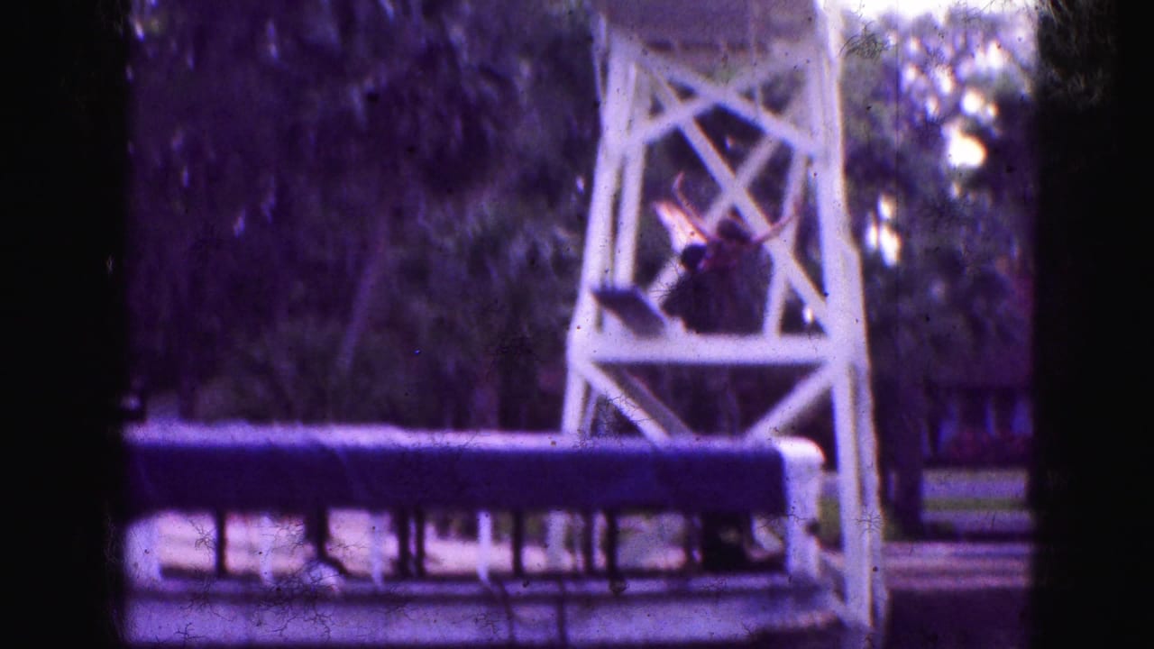 1975 Florida Everglades home-movie frame showing a white wooden lookout tower by a canal, with a small figure positioned near the structure.