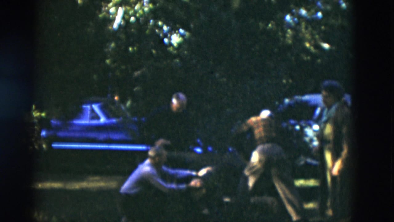 Older adults on a shaded lawn in Somerset, Kentucky, 1975, with parked cars and trees visible in soft 8mm footage.