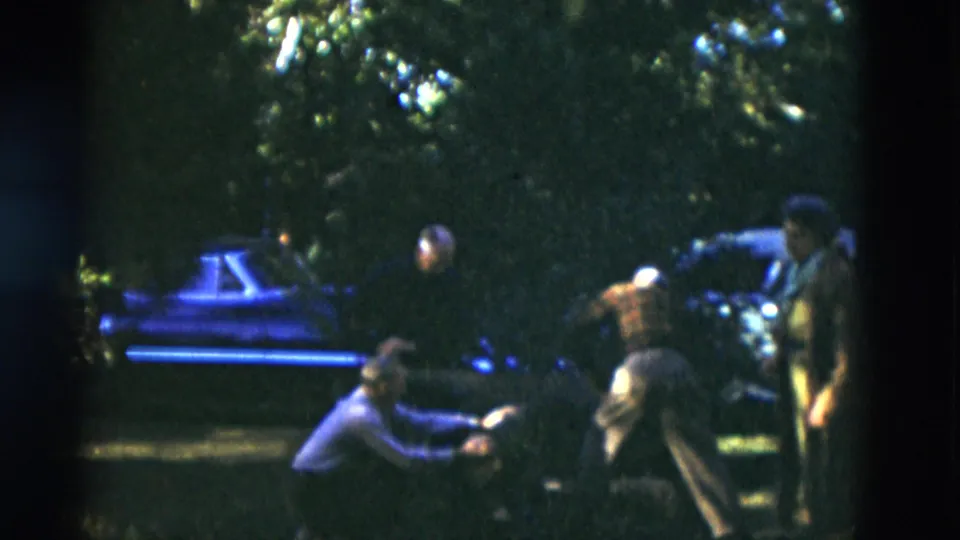 Older adults on a shaded lawn in Somerset, Kentucky, 1975, with parked cars and trees visible in soft 8mm footage.