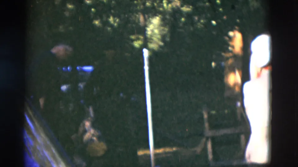 1975 Somerset, Kentucky frame with a man in a light shirt near a dark vehicle and wooded background.