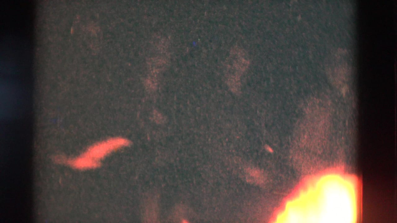 1975 Somerset, Kentucky home-movie frame with a bright campfire flare at lower right and dim red-orange detail in darkness.