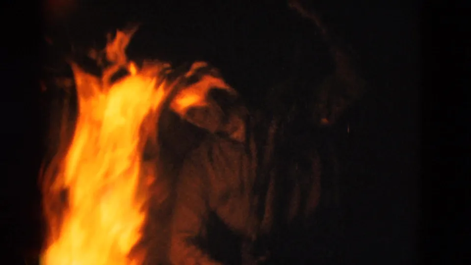 1975 Somerset, Kentucky home-movie frame showing campfire flames lighting a bundled person in a dark nighttime gathering.