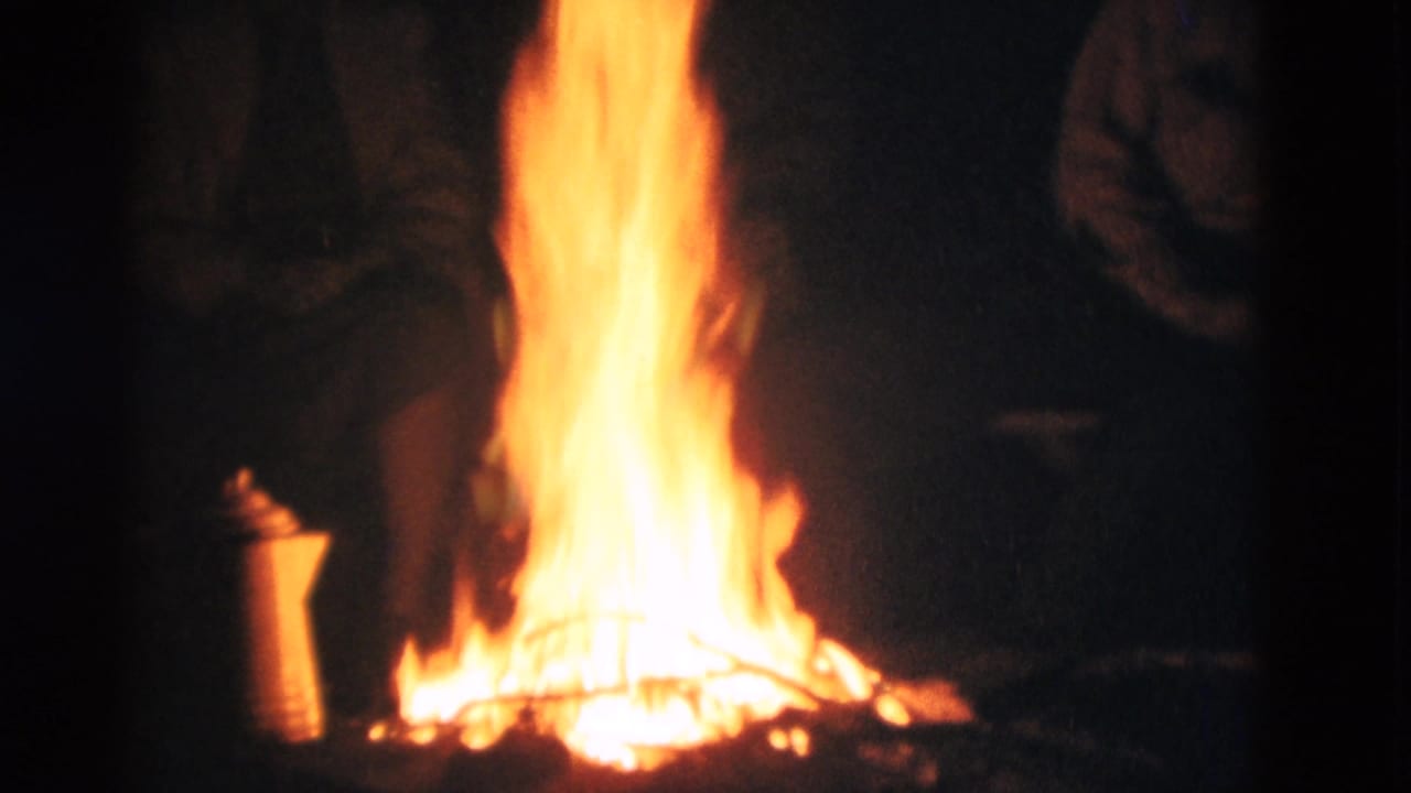 Bright campfire burning at night with dark silhouetted figures nearby.