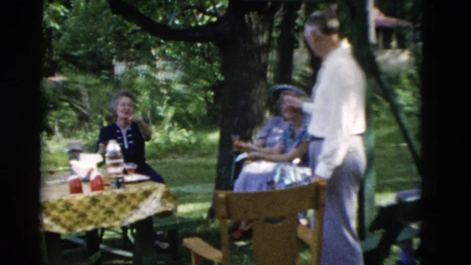 1975 Somerset, Kentucky frame with adults seated and standing around a picnic table in a leafy backyard.