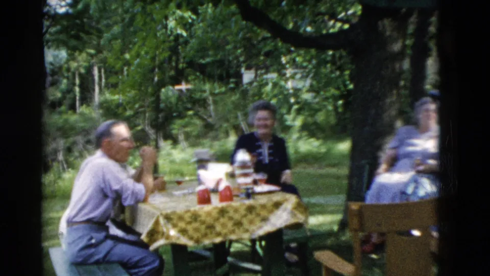 1975 Somerset, Kentucky frame showing a seated man gesturing at a backyard picnic with women seated nearby.