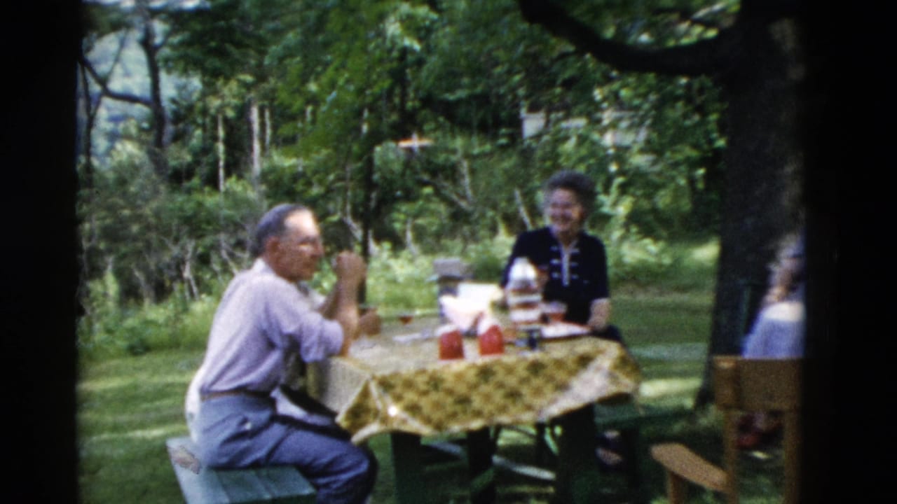 1975 Somerset, Kentucky 8mm frame showing older adults around a picnic table with a yellow patterned cloth in a wooded yard.