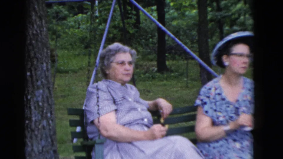 In Somerset, Kentucky home-movie footage from 1975, two women in patterned dresses sit on a green bench in a wooded park.
