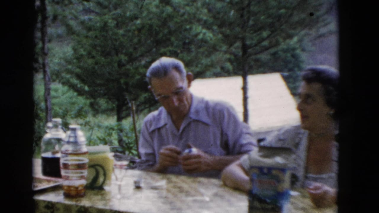 In 1975 Somerset, Kentucky home-movie footage, an older man in glasses sits beside a woman at an outdoor table with drink containers.