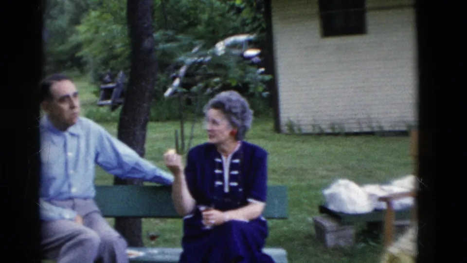 A seated couple appears to converse on a bench during the 1975 Somerset, Kentucky outdoor reunion, with trees and a parked car behind them.