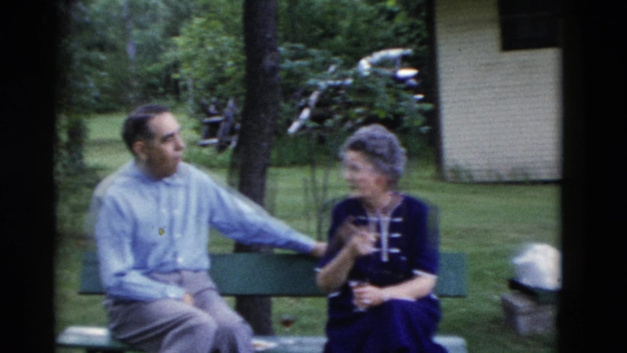 Man and woman seated on a green bench in a leafy yard.