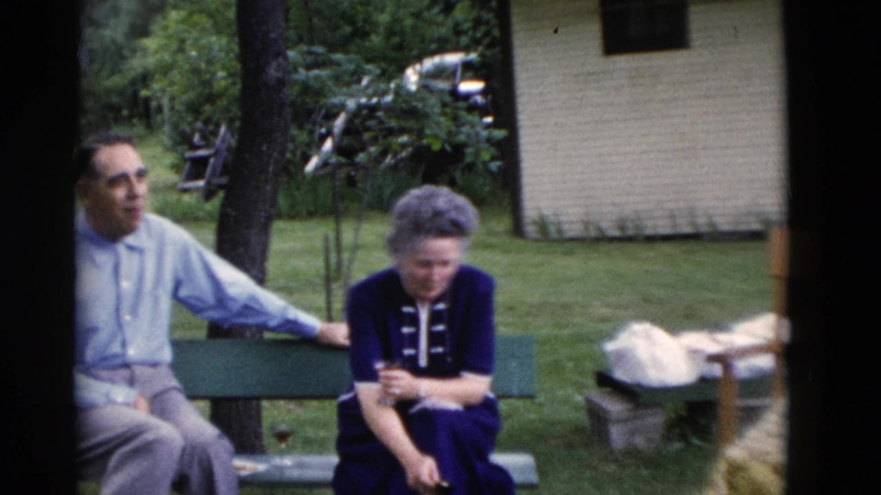 Older man and woman seated on a green bench in a grassy yard.