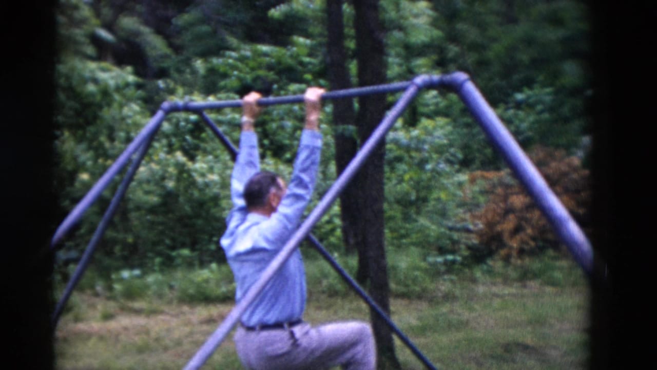 1975 8mm frame from Somerset, Kentucky showing a man using a homemade pull-up bar among trees and grass.