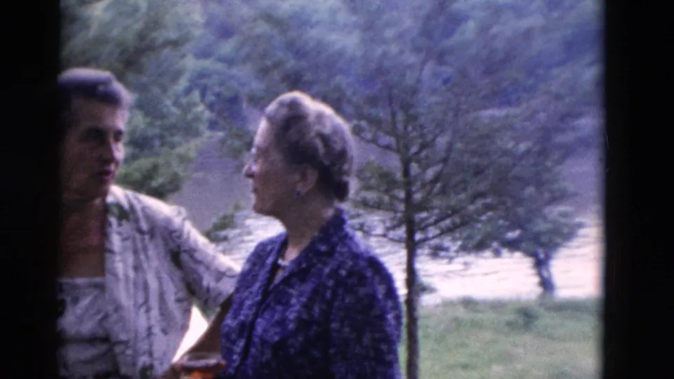 Candid 1975 8mm view of two adult women talking outdoors in Somerset, Kentucky, with trees and grass behind them.