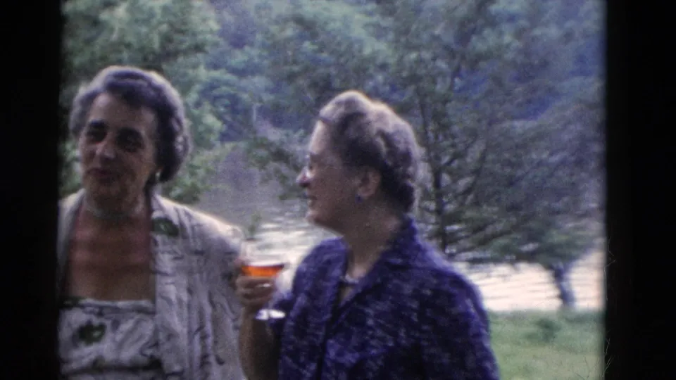 Somerset, Kentucky 1975 home-movie frame showing two women in patterned clothing chatting outdoors beside trees and water.