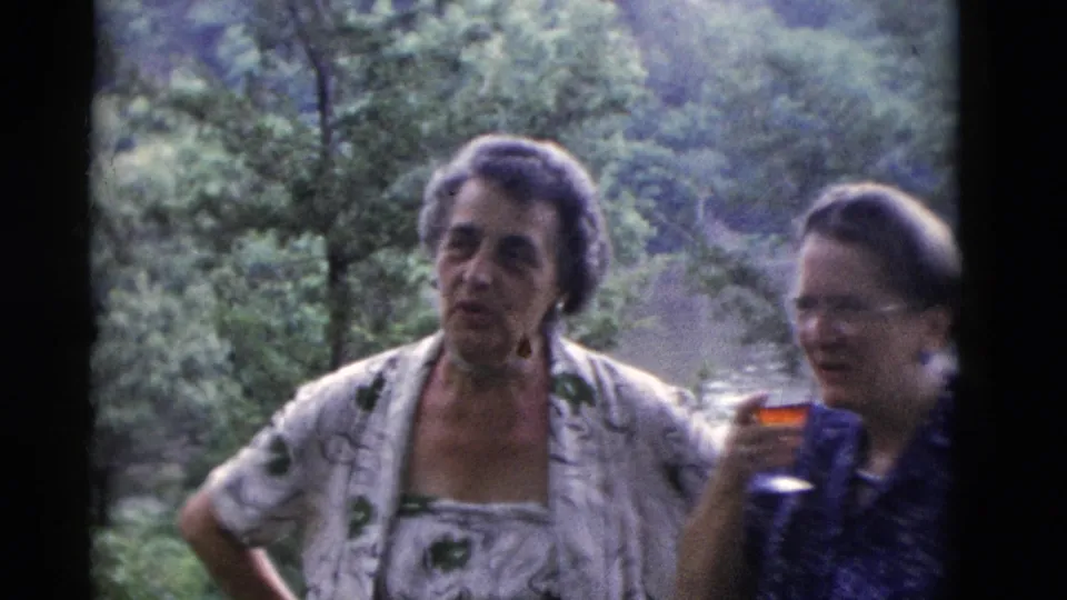 Somerset, Kentucky 1975 frame of women outdoors at a wooded gathering, with a drink glass visible and soft 8mm motion blur.