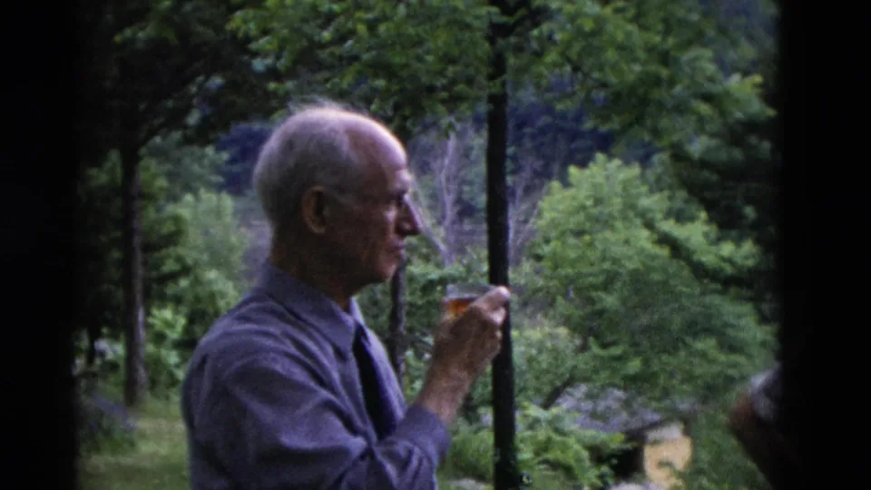 An older man holds a drink glass in a wooded Somerset, Kentucky setting in metadata-supported 1975 home-movie footage.