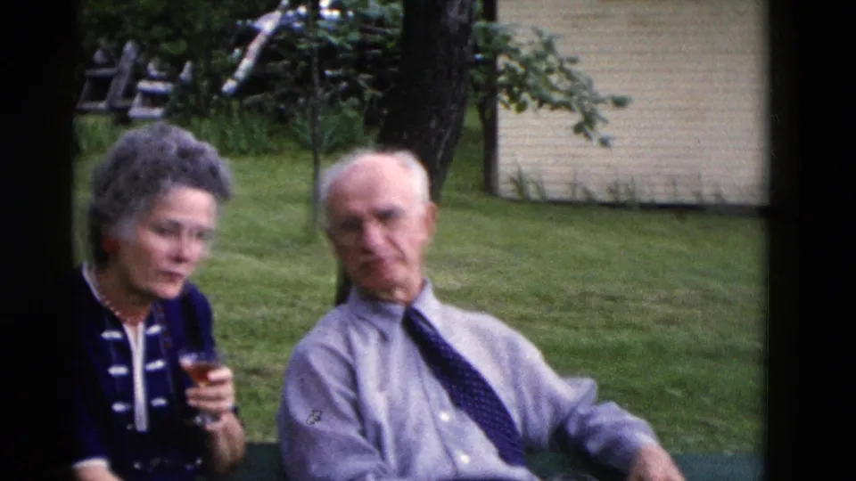 Older woman in a dark dress with white trim holds a drink beside an older man in a Somerset, Kentucky yard in 1975.