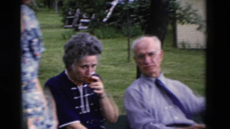 Older woman sips from a glass while seated beside an older man in the 1975 Somerset, Kentucky outdoor gathering.