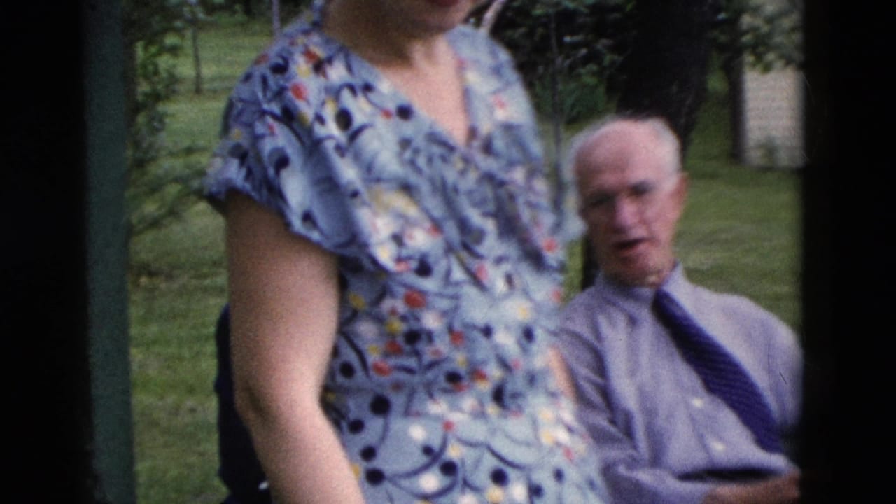 In 1975 Somerset, Kentucky home-movie footage, a floral-dressed woman stands in the foreground while an older man sits in a grassy yard.