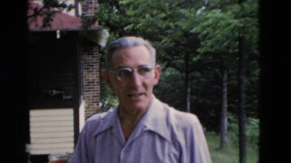 An older man with glasses faces the camera on a grassy lawn, with a house and wooded background visible in the 1975 Kentucky footage.