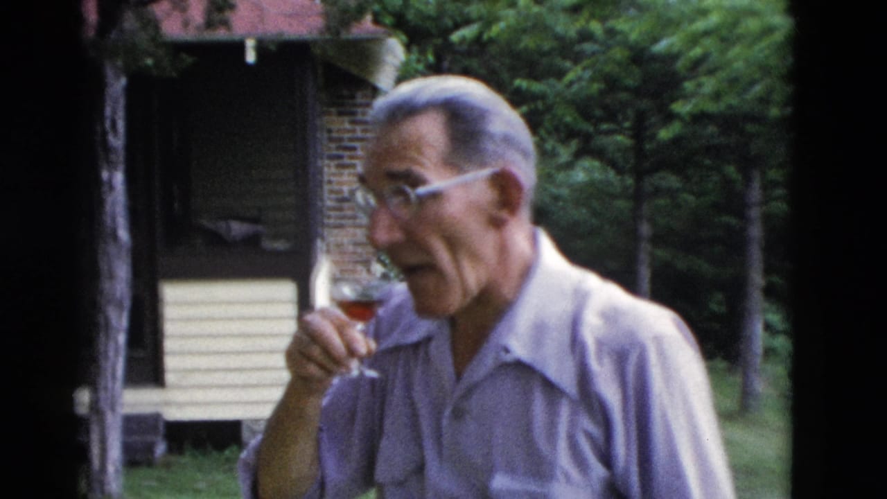 Older man in glasses and a light shirt sips a red drink outdoors near a rustic cabin in Somerset, Kentucky, 1975.