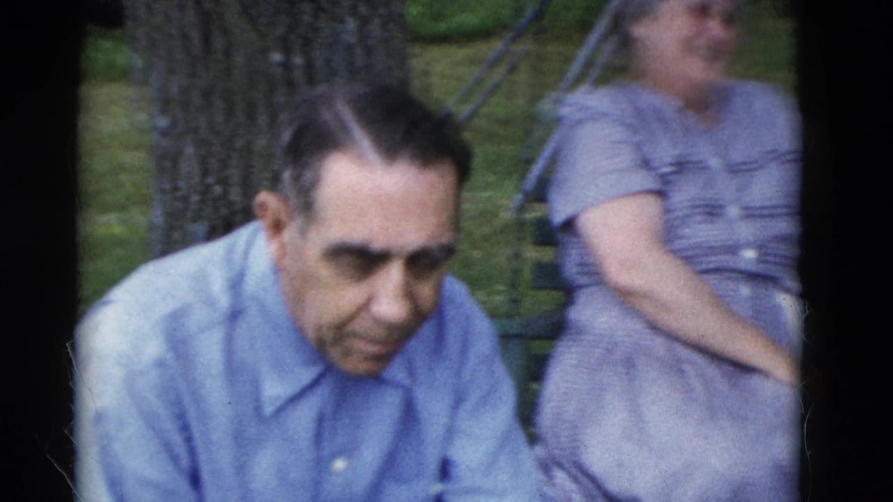 In the Somerset, Kentucky 1975 home movie, an older man sits in a wooded park while a woman on a swing appears behind him.